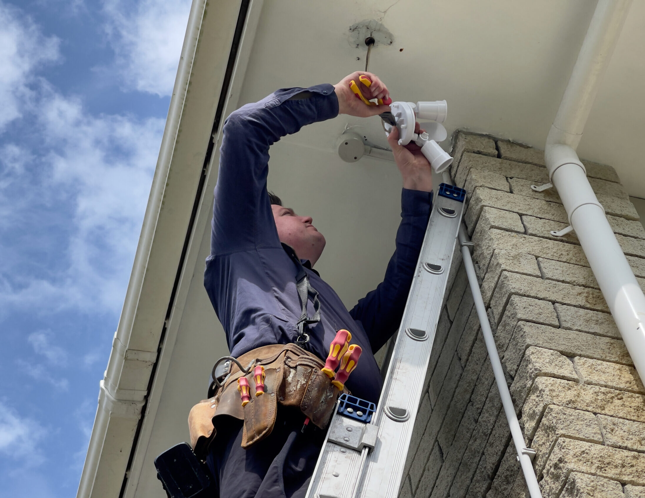 Repairman installing a double LED light on the corner of a 1980's house